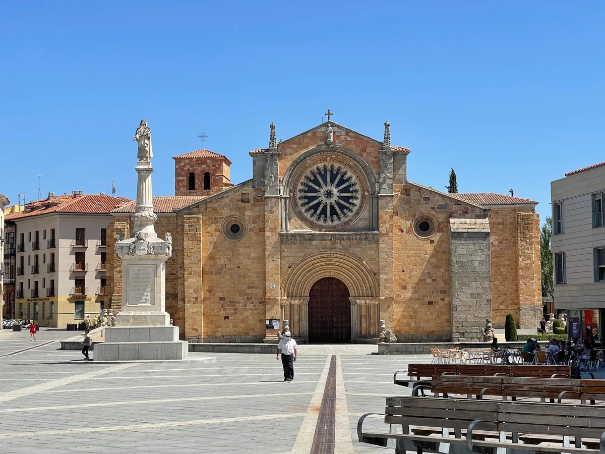 A granite west front with a rose window and a column monument in the square before it.