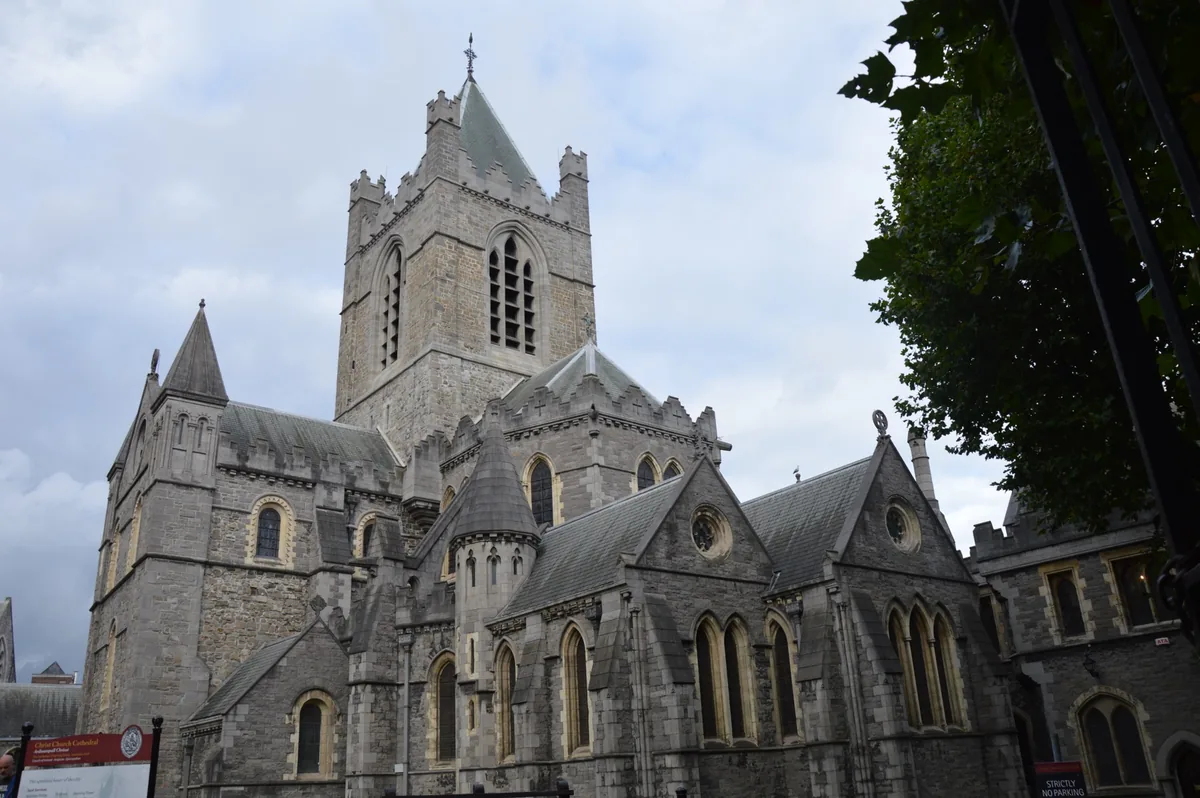 A grey stone cathedral with a square tower and flying buttresses rising above a lawn.