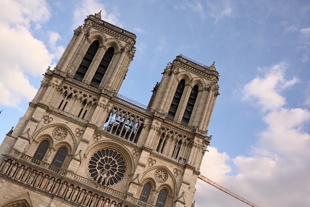 The twin-towered west front with its three portals and rose window under a cloudy sky.