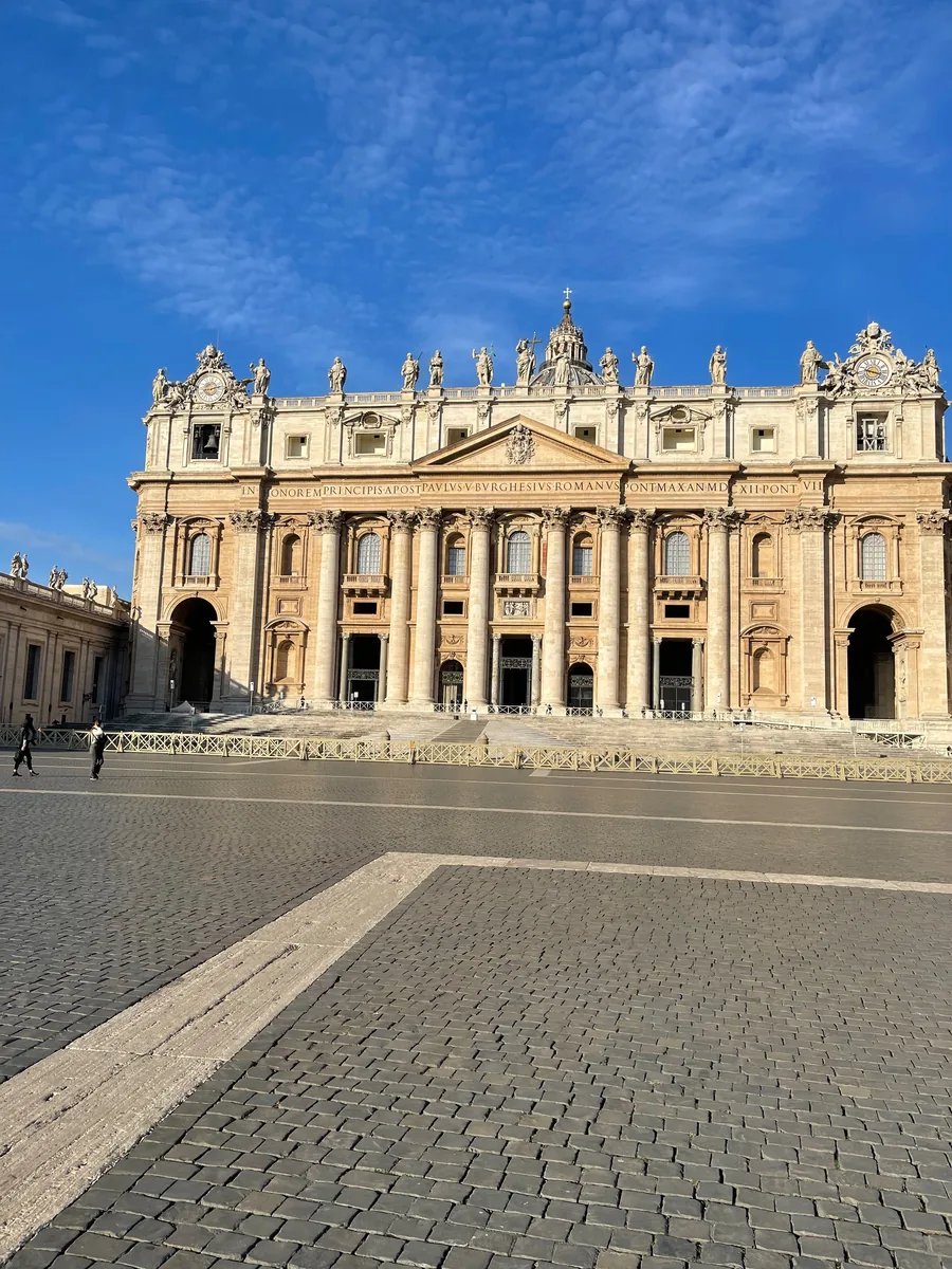The façade of the basilica seen across St. Peter's Square in early morning light, with the paving empty and the dome behind the attic.